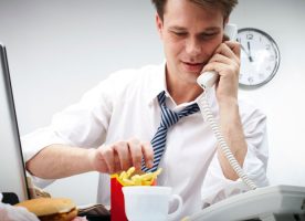 Oificinista come papas fritas sentado en su escritorio mientras habla por teléfono.