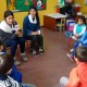 Dos estudiantes desarrollan un trabajo grupal con los niños sentados en círculo.