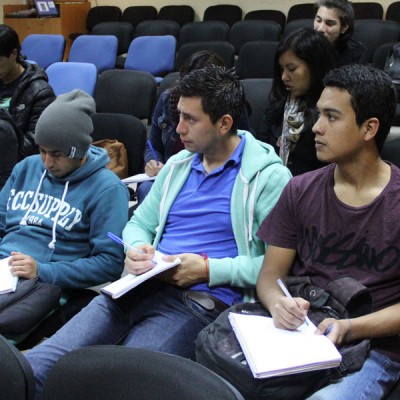 Tres estudiantes escuchan y toman apuntes durante la actividad.