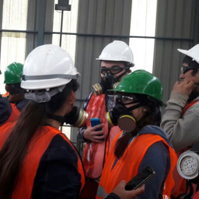 Estudiantes dentro de planta con mascarillas, cascos y chaquetas reflectantes.