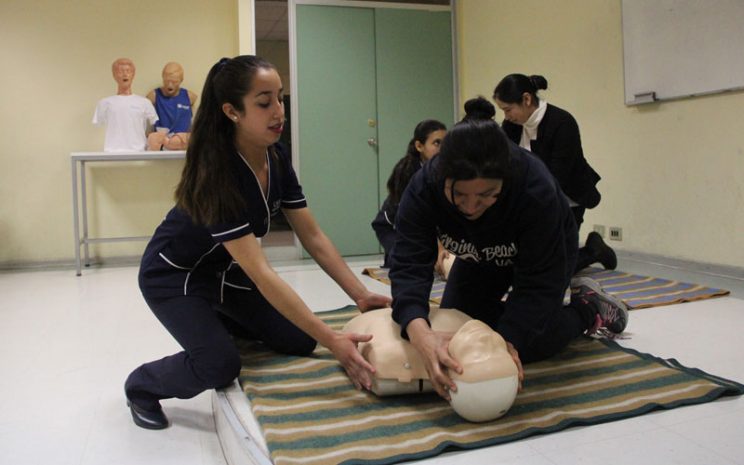 Estudiante de Enfermería enseña a una participante técnicas de reanimación con un muñeco.