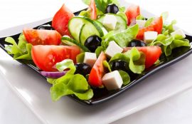 Plato de ensalada con verduras verdes, tomates, aceitunas y queso.