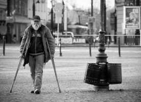 Foto de un adulto mayor caminando con muletas en la calle.