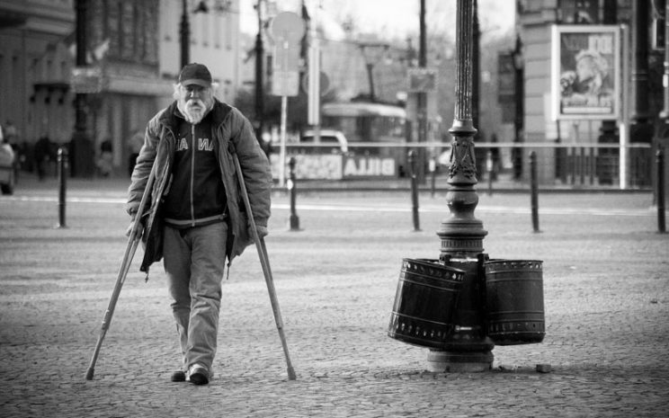 Foto de un adulto mayor caminando con muletas en la calle.