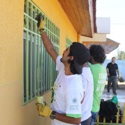 Grupo de estudiantes pintan protecciones de ventanas.