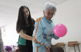 Adulta mayor es apoyada por una alumna de Kinesiología durante un ejercicio con balón.