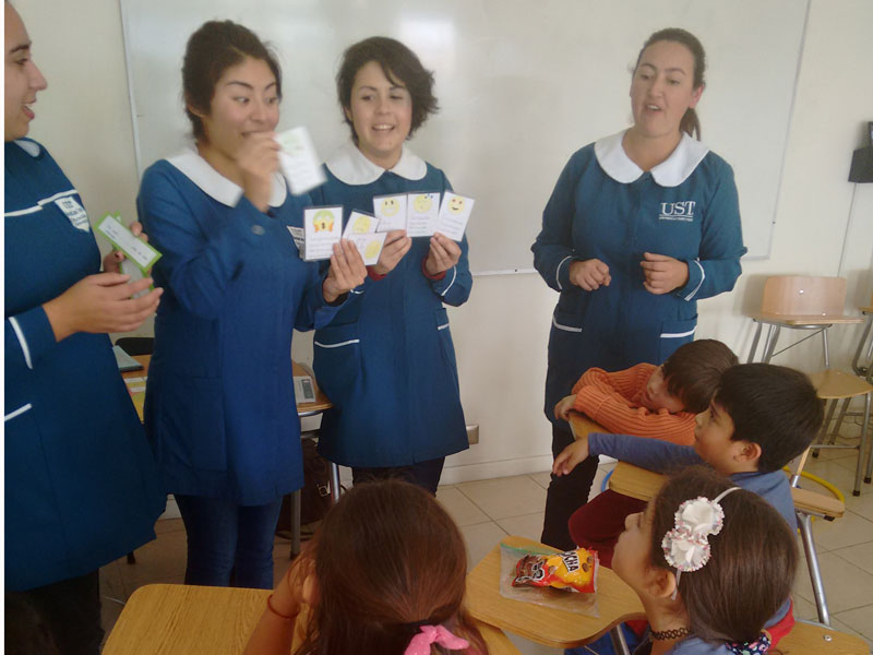 Cuatro niños observan tarjetas que les muestran dos estudiantes de Educación Diferencial.