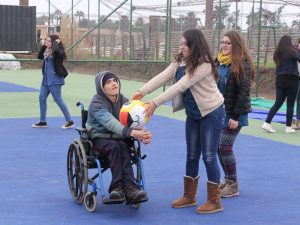 Niño en silla de ruedas recibe un balón de parte de una alumna de Educación Diferencial.