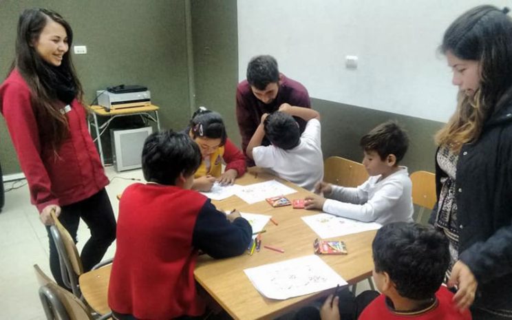 Tres estudiantes de Psicología supervisan trabajo grupal de 5 niños.