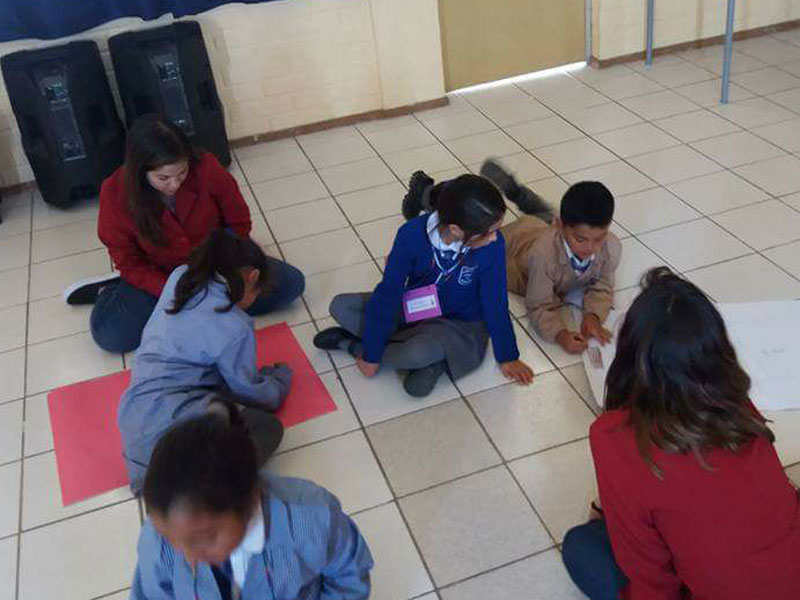 Niños dibujan en el suelo, mientras observan dos alumnos de Psicología.
