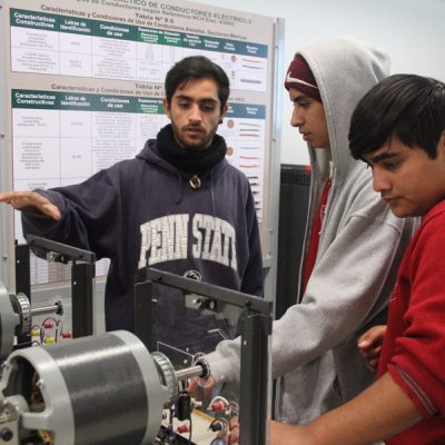 Estudiante muestra motores eléctricos a dos estudiantes.