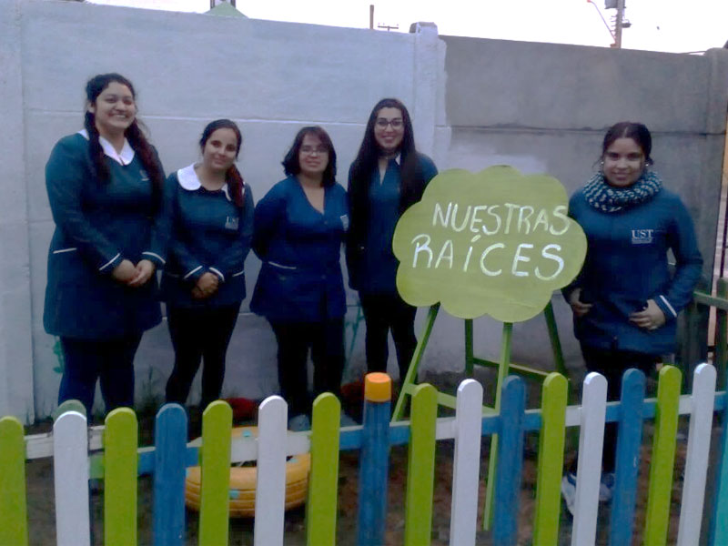 Cinco alumnas junto a cartel que dice Nuestras raíces.