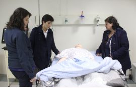Tres de las enfermeras observan maniquí de enfermo acostado en camilla.