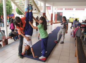 Alumna realizando posición invertida con ayuda de compañera y su profesora. 