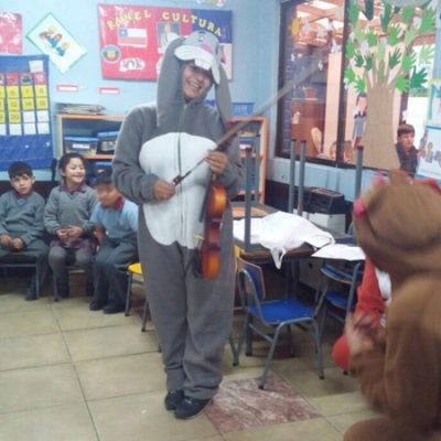 Dos estudiantes disfrazadas de conejo y oso, realizan una obra de teatro a niños y niñas en una sala de clases.