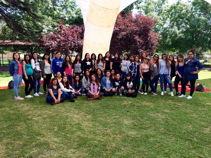 Alumnas del área de educación agrupados en la cancha de pasto, bajo un toldo blanco.