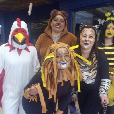 Cinco estudiantes disfrazadas de gallo, león, oso, tigre y abeja, posan sonriendo frente la cámara.