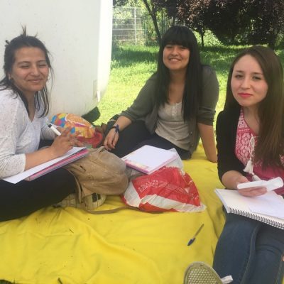 Tres alumnas están sentadas sobre una manta amarilla, en el pasto, mientras realizan una encuesta.