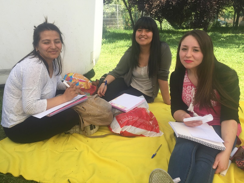 Tres alumnas están sentadas sobre una manta amarilla, en el pasto, mientras realizan una encuesta.