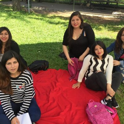 Cinco alumnas están sentadas sobre una manta roja, en el pasto, mientras realizan actividades de autoevaluación.