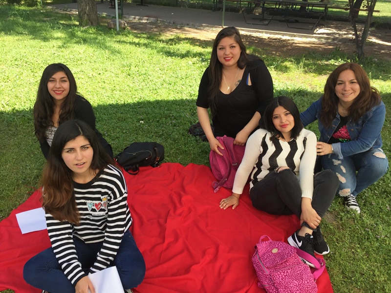 Cinco alumnas están sentadas sobre una manta roja, en el pasto, mientras realizan actividades de autoevaluación.