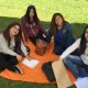 Cuatro alumnas están sentadas sobre una manta de color anaranjado, en el pasto, mientras realizan actividades de autoevaluación.