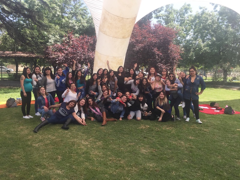 Alumnas del área de educación agrupados en la cancha de pasto, bajo un toldo blanco.